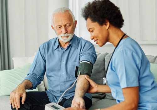 Doctor or nurse caregiver with senior man using blood pressure tool at home or nursing home
